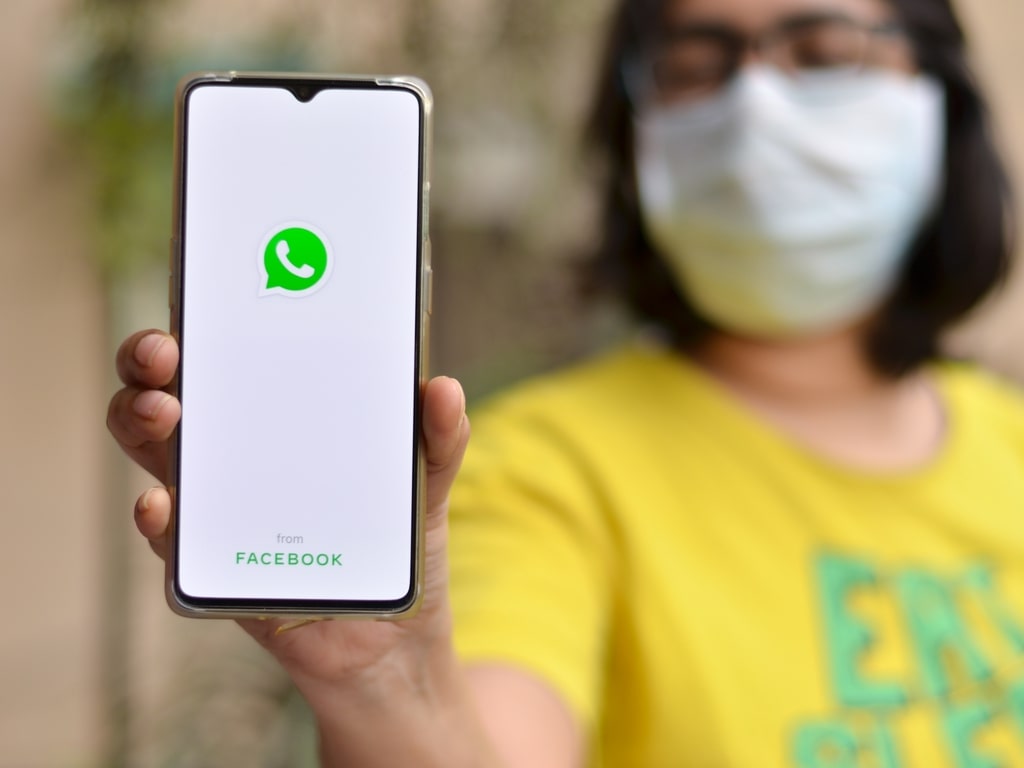 mulher de máscara com celular na mão mostrando o whatsapp